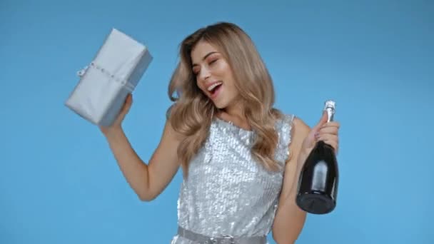 glimlachende vrouw dansen met champagne en geschenk geïsoleerd op blauw  - Video