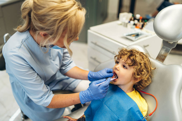 Cute young boy visiting dentist, having his teeth checked by female dentist in dental office - Photo, Image