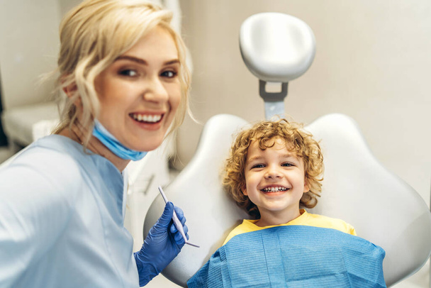 Cute young boy visiting dentist, having his teeth checked by female dentist in dental office - Foto, Imagem
