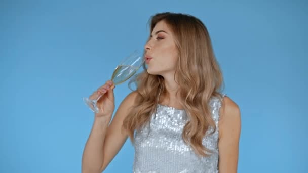 Mujer sonriente bebiendo champán aislado en azul  - Metraje, vídeo
