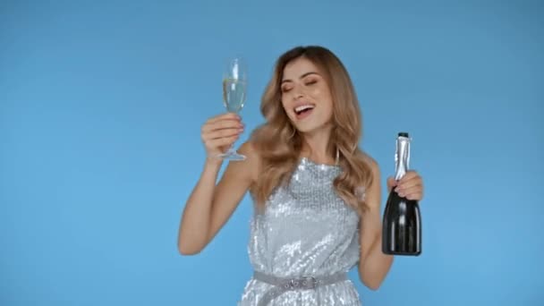 Женщина танцует со стаканом и бутылкой шампанского изолированы на синий  - Кадры, видео