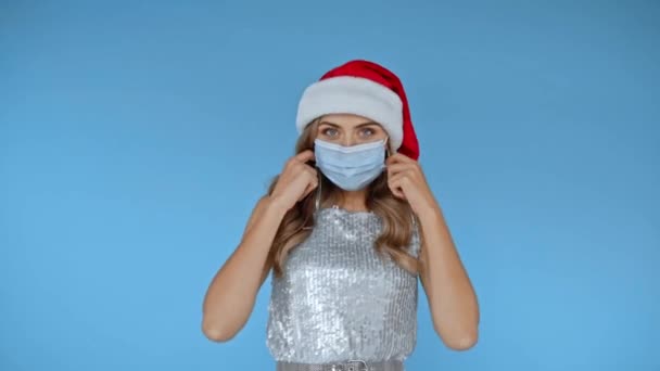 Kobieta w czapce Mikołaja rzuca maską medyczną odizolowaną na niebiesko  - Materiał filmowy, wideo