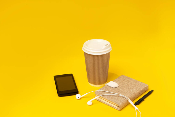 Bastelglas, Telefon, Notizblock und Kopfhörer auf gelbem Hintergrund. - Foto, Bild