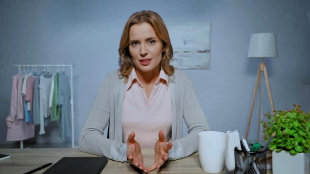 pozytywna kobieta gestykulująca i rozmawiająca przy stole podczas skype call w domu - Materiał filmowy, wideo