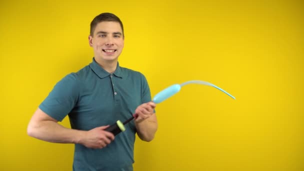 Een jongeman blaast een lange blauwe ballon op met een pomp op een gele achtergrond. Man in een groene polo. - Video