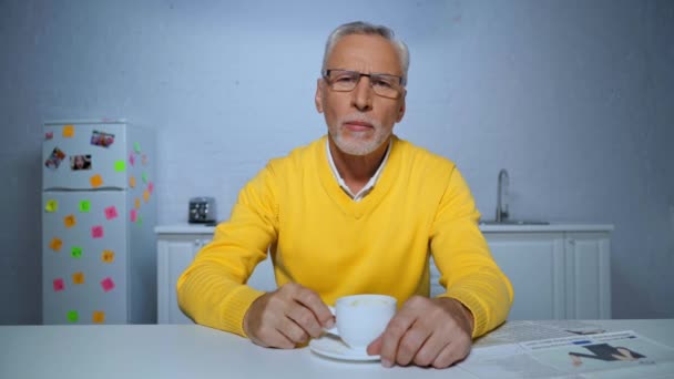 keskittynyt keski-ikäinen mies juo kahvia ja puhuu aikana skype puhelun kotona - Materiaali, video