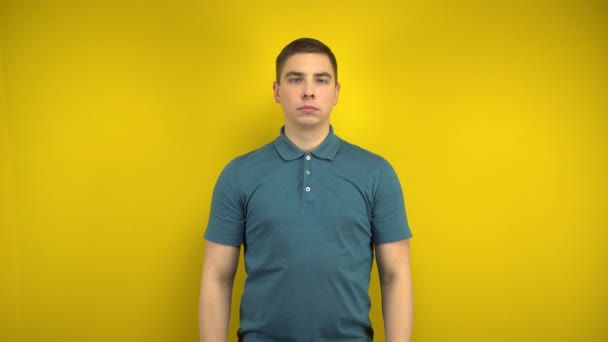 A young man makes a sad and cheerful smile on his face with her fingers on a yellow background. Man in a green polo. - Footage, Video