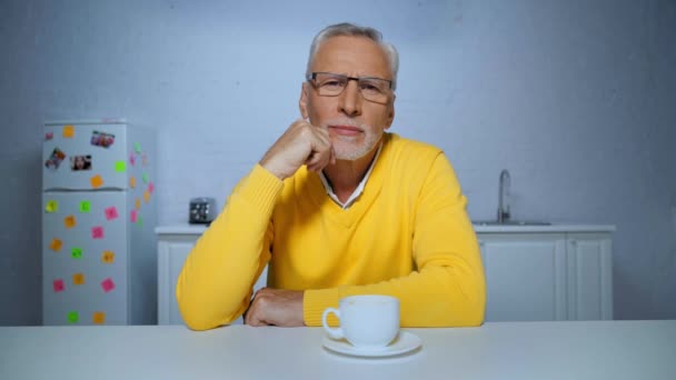 enfocado hombre de mediana edad bebiendo café, mirando a la cámara y hablando en casa - Imágenes, Vídeo