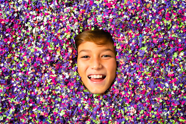 Nuori poika hymyilevä kasvot ympäröivät värillinen konfetti - Valokuva, kuva
