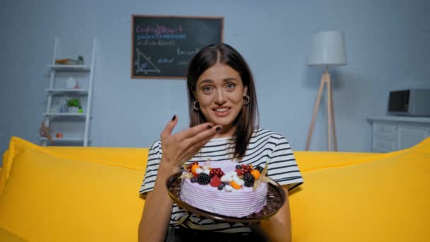 allegra giovane donna con torta parlando e gesticolando durante la chiamata skype a casa - Filmati, video