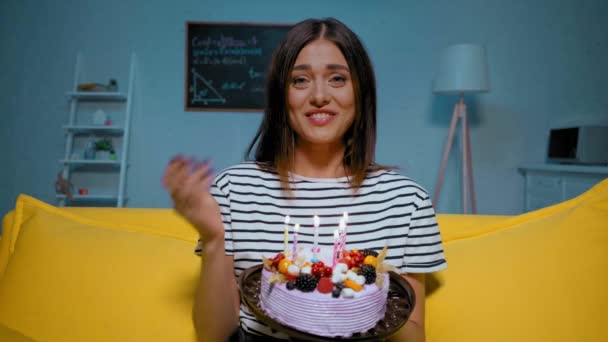 счастливая молодая женщина с тортом на день рождения, разговаривая и задувая свечи дома - Кадры, видео