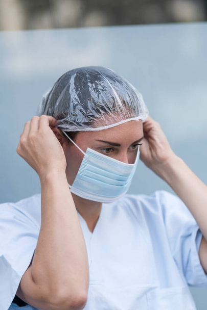 Portrait of a woman doctor putting on and fixing her surgical protective mask before her work shift - Fotó, kép