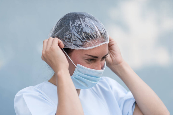 Портрет женщины-врача, надевающей и чинящей свою хирургическую защитную маску перед рабочей сменой - Фото, изображение