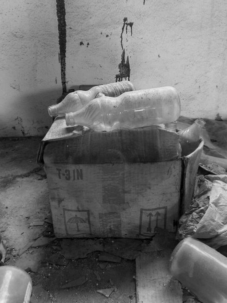 Una vecchia scatola di cartone sporco con bottiglie di vetro polveroso in un edificio disordinato abbandonato. - Foto, immagini