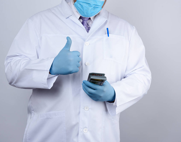 lekarz w białym płaszczu, w niebieskich jałowych rękawiczkach, trzyma paczkę papierowych pieniędzy, łapówkę i zapłatę za wykonaną pracę - Zdjęcie, obraz