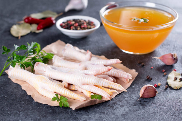 Chicken broth and chicken feet with vegetables, spices and herbs on gray background. Natural collagen of animal origin - Photo, Image