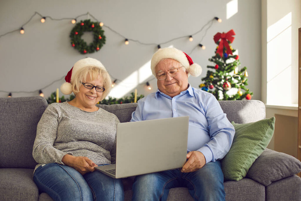 Smiling senior couple sitting on sofa at home and video calling family using laptop - Fotoğraf, Görsel