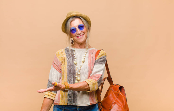 middle age woman smiling cheerfully, feeling happy and showing a concept in copy space with palm of hand - Fotoğraf, Görsel