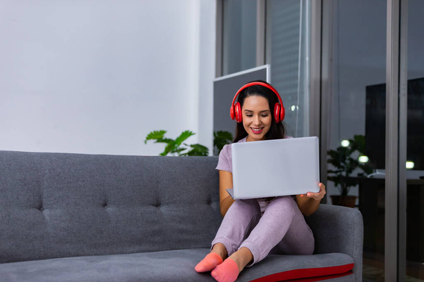 Szczęśliwe kobiety noszące słuchawki za pomocą laptopa siedzącego na kanapie w nocy w domu - Zdjęcie, obraz