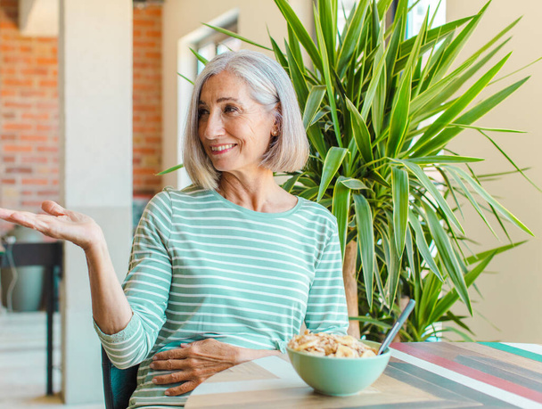 жінка середнього віку усміхається весело, відчуває себе щасливою і показує концепцію в копіювальному просторі з долонею руки
 - Фото, зображення
