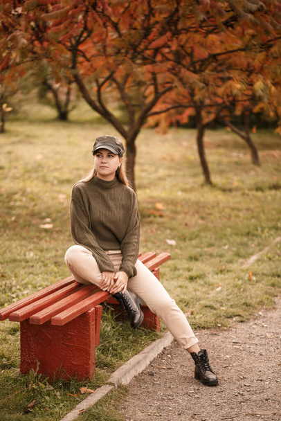 Молода красива дівчина, одягнена в стильний одяг, зелений светр і бежеві штани, в осінньому парку з красивими деревами
 - Фото, зображення