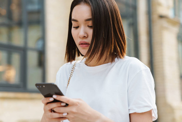 junge schöne asiatische Frau mit Telefon, während zu Fuß auf einer Straße - Foto, Bild