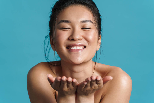Piękny portret uśmiechniętej topless młoda azjatycka kobieta pozowanie stojąc odizolowany na niebieskim tle, wysyłanie pocałunek - Zdjęcie, obraz