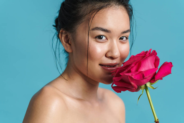 Image of pleased shirtless asian girl posing with rose isolated over blue background - Foto, Bild