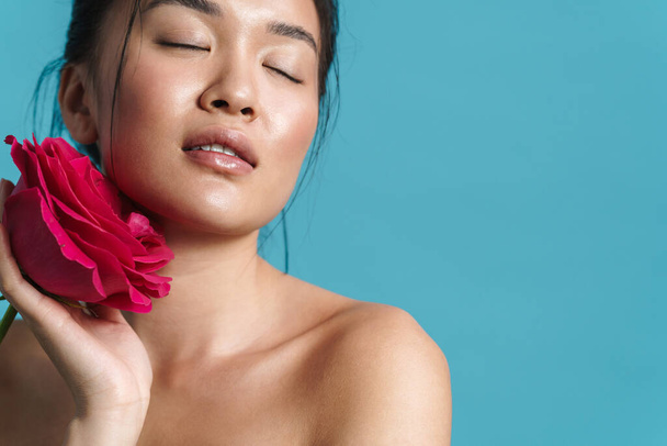 Image of pleased shirtless asian girl posing with rose isolated over blue background - Photo, Image