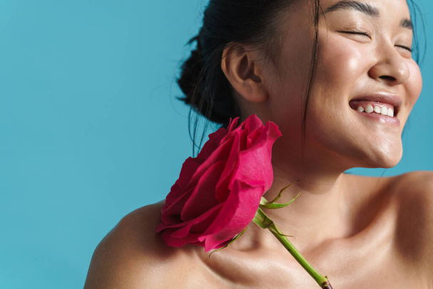Kép félmeztelen ázsiai lány mosolyog, miközben pózol rózsa elszigetelt kék háttér - Fotó, kép