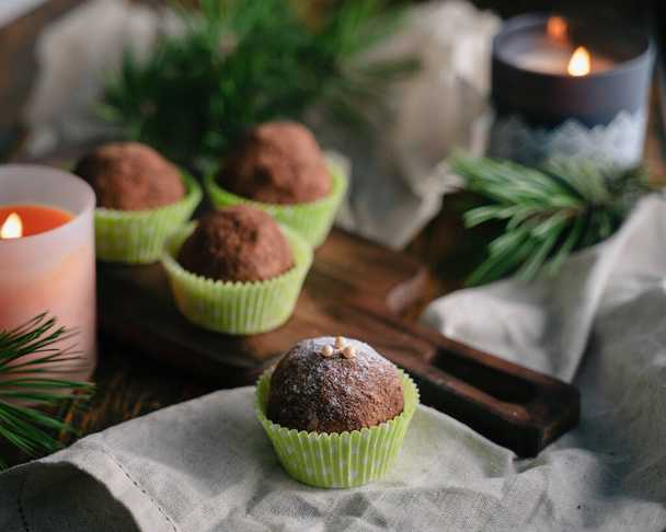 Rum balls with powdered sugar on a wooden cutting Board, next to candles and pine twigs on a wooden table - Photo, Image