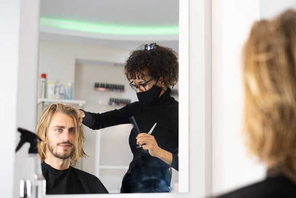 Positif jeune coiffeur noir appréciant de travailler dans un salon de beauté et de séchage des cheveux du client - Photo, image