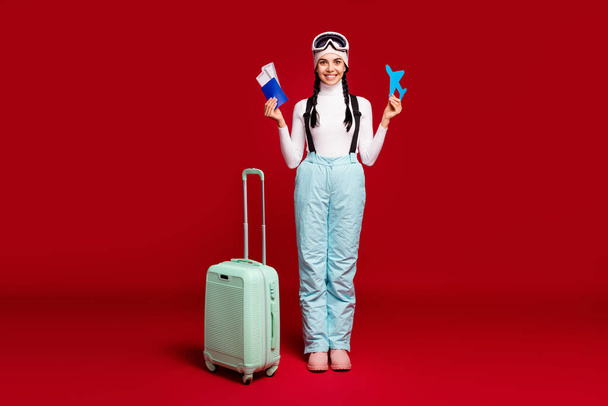 Fulll size photo of young happy girl with tails hold passport wear blue pants leaving for winter vacation isolated on red color background - Zdjęcie, obraz
