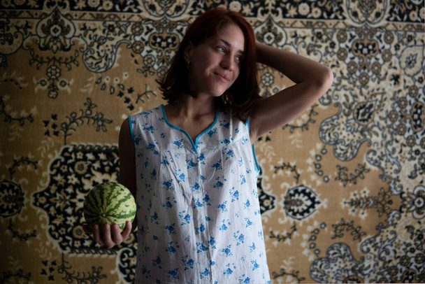 Red Hair Caucasian Girl in Chintz nightgown Sleepwear holding Little Watermelon with the Soviet Carpet on Background - Photo, Image