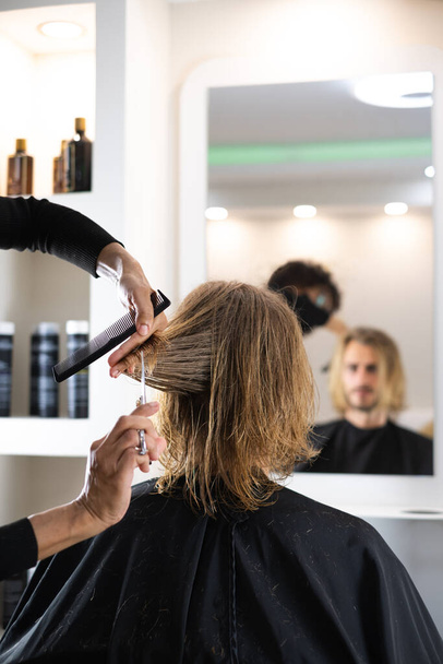 Beau client blond masculin se faire couper les cheveux par une coiffeuse noire - Photo, image