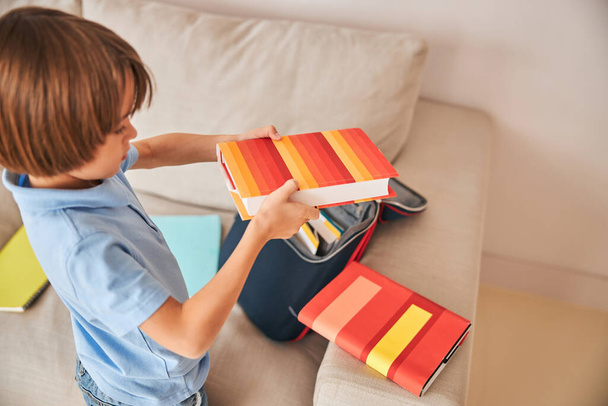 Kleiner Junge packt Tasche aus und hält Bücher in der Hand - Foto, Bild
