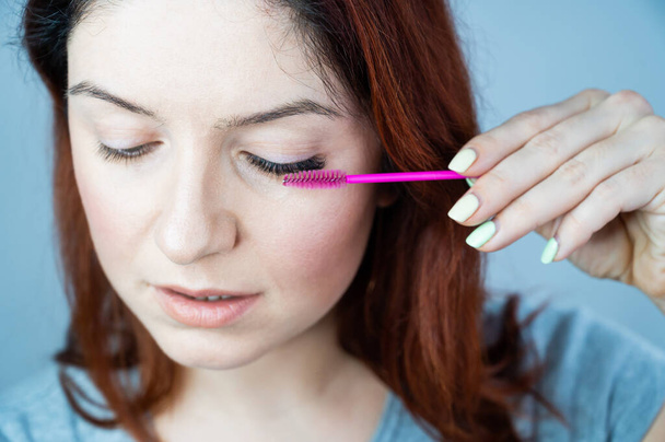 Red head woman brushing her extension eyelashes with a brush. girl with impending eyelid make-up mascara. Beauty industry.  - Photo, Image