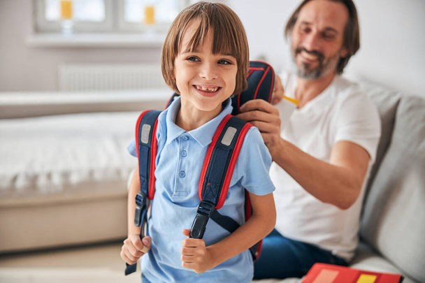 Glückliches Kind mit Rucksack, das neben seinem fröhlichen Vater steht - Foto, Bild
