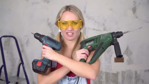 Funny woman holding construction tools on the background of repairs in the house - Footage, Video