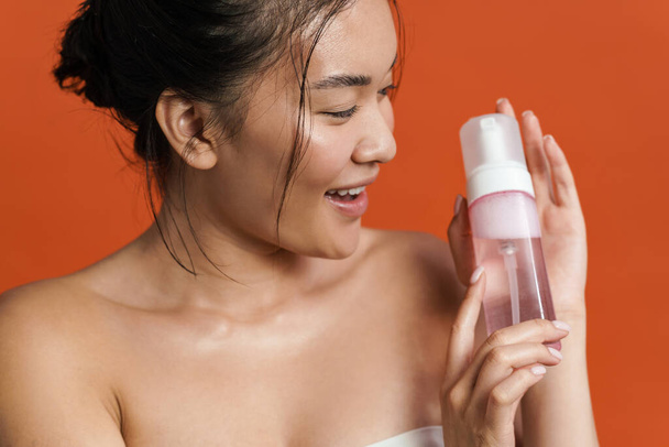 Image of smiling shirtless asian girl posing with cleansing foam isolated over orange background - Фото, зображення