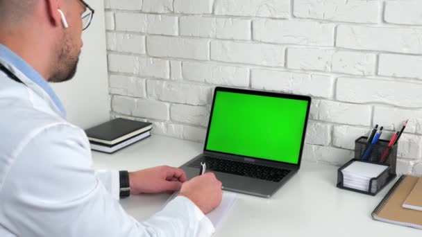 緑の画面のラップトップを探している医師は、患者がノートブックに症状を書きます - 映像、動画