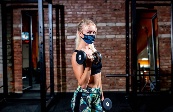jonge vrouw in bescherming masker doen fitness oefeningen in de sportschool - Foto, afbeelding