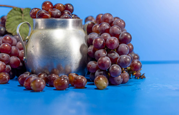 Frutos de uva. Ingrediente para sucos e vinho. Bagas de uva em recipiente de alumínio. Fundo azul. Alimentação humana - Foto, Imagem
