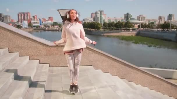 Volledig shot van jonge slanke vrouw in hoofdtelefoon springen touw springen op de trap bij outdoor workout - Video
