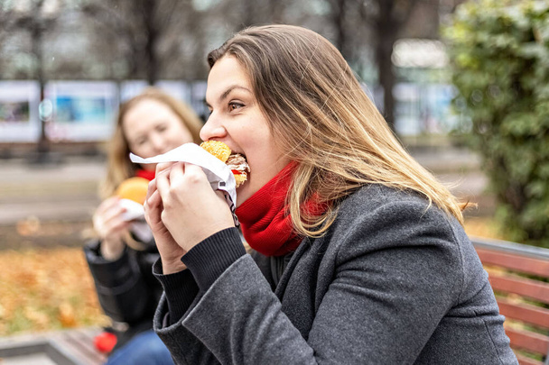 Young hungry woman eats Burger and takes lunch break outdoors in Park.Fast food. Takeaway food concept. - Photo, Image