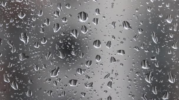 Krople deszczu spadające na szybę okienną na niewyraźne tło domu w deszczowy pochmurny dzień. Krople różnej wielkości odzwierciedlają sąsiedni budynek mieszkalny - Materiał filmowy, wideo