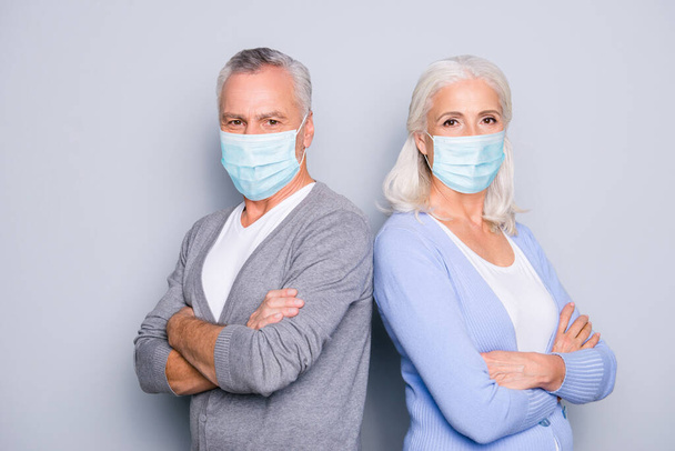 Photo portrait of old man and woman standing back to back with folded arms wearing blue face masks isolated on grey colored background - Fotó, kép