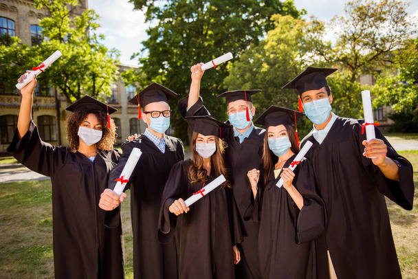 Photo portrait of six students celebrating graduation with diplomas in hands wearing face masks outdoors - Foto, immagini