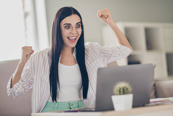 Photo of young amazed business woman raise fists open mouth wear spectacles shirt in home workstation indoors - Foto, afbeelding