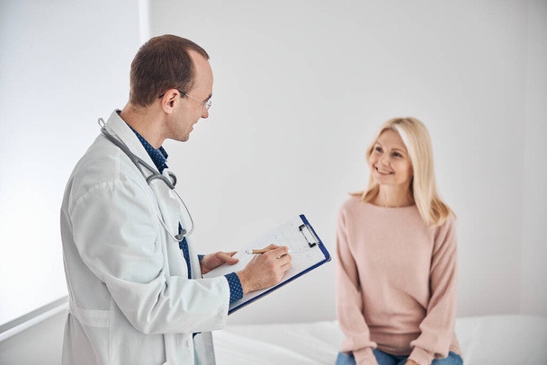 Smiling dark-haired physician interviewing the beautiful female patient - Foto, Bild